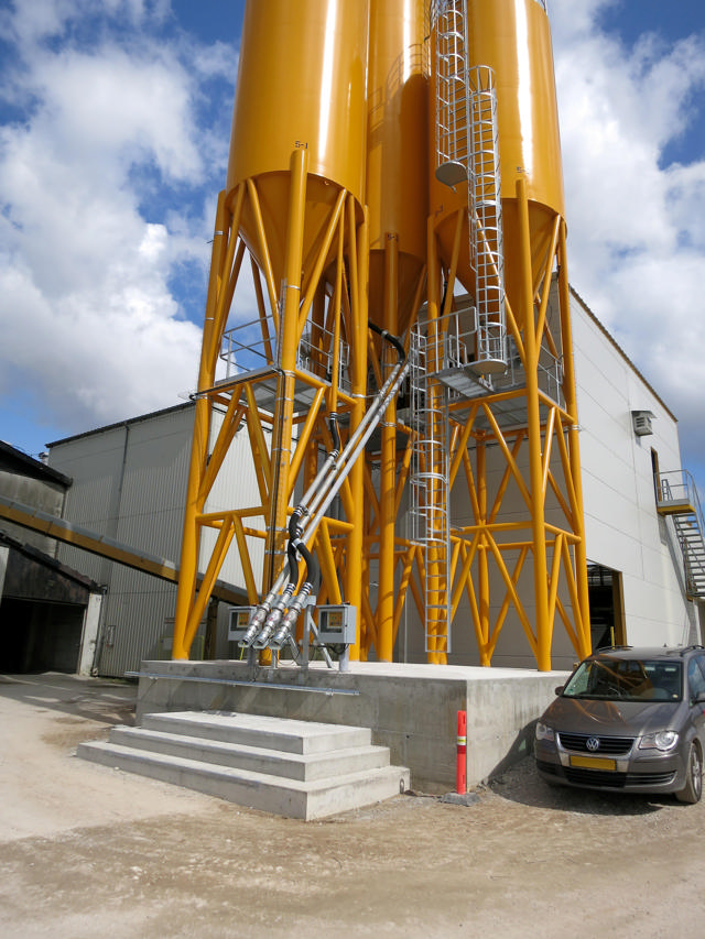 Three orange cement silos outside a factory.